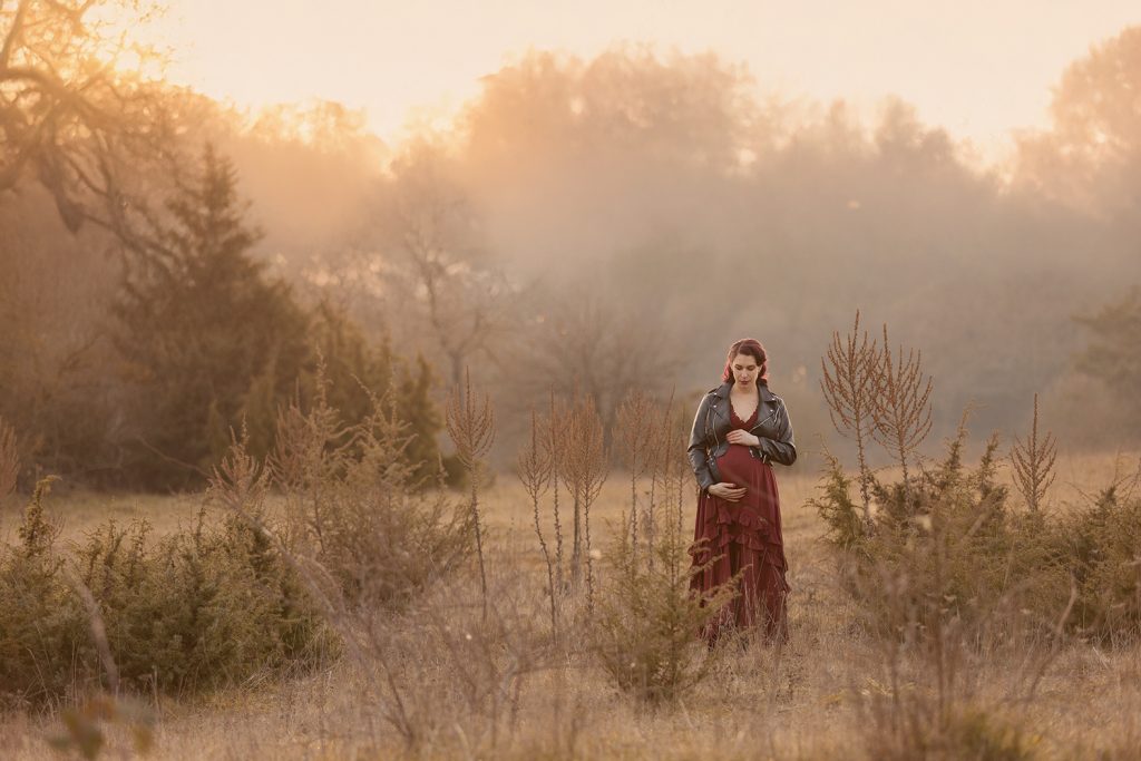 Schwangere Frau in weinrotem langem Kleid und Lederjacke läuft duch wunderschöne wilde Kulisse, eine Bild aus ihren Babybauch Shooting Stuttgart