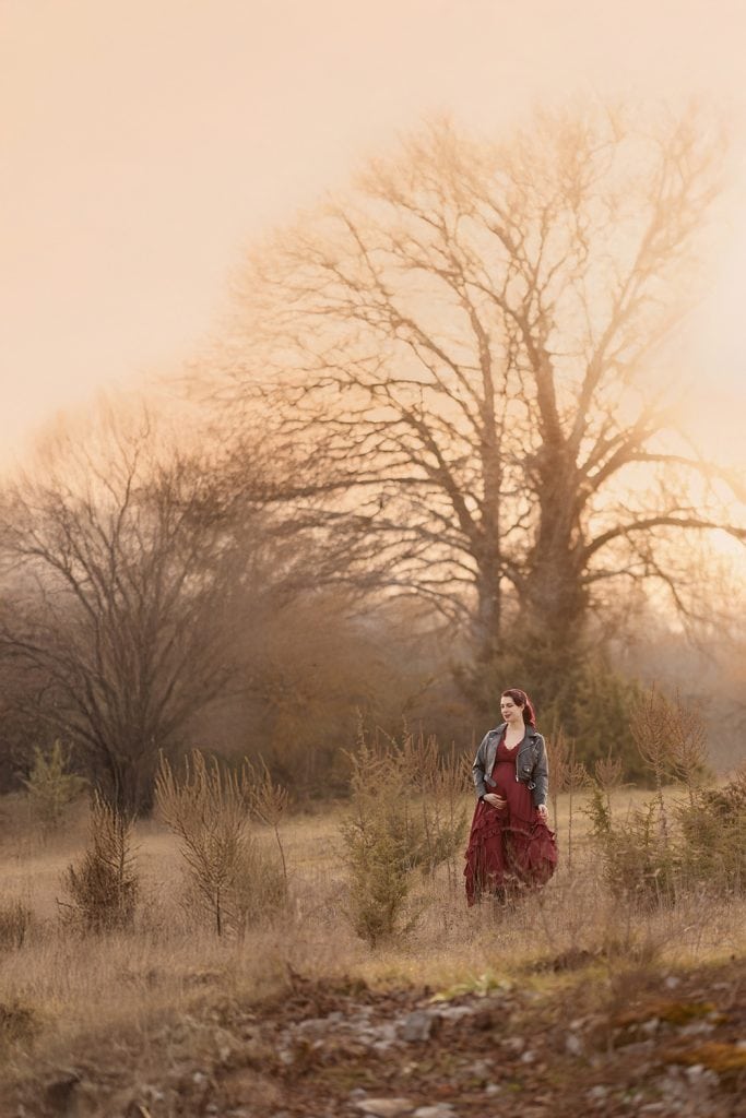 Schwangere Frau mit roten Haaren in rotem Kleid und Lederjacke im Abendlicht auf einer Wiese, stimmungsvolle Outdoor-Fotografie in Herrenberg