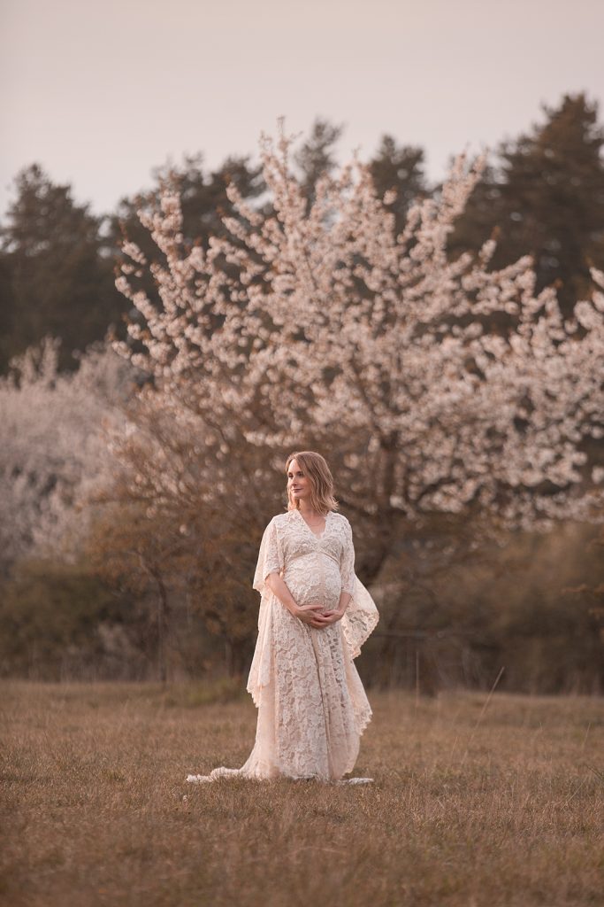 Schwangere Frau in weißem Spitzenkleid vor einem Blühenden Baum, bild ist bei einem Babybauch-Shooting in Tübingen entstanden im Frühling