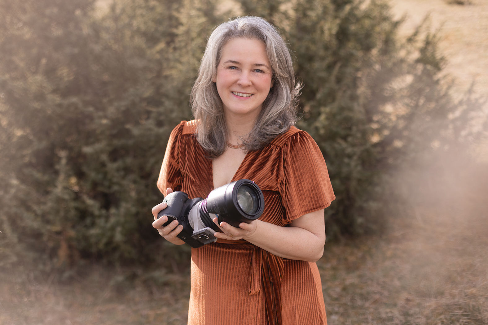 Sonja Auer, Fotografin in Stuttgart, lächelt in die Kamera im kupferfarbenen Samtkleid und hält ihre Kamera in der Hand – Fotoshooting Preise & Pakete