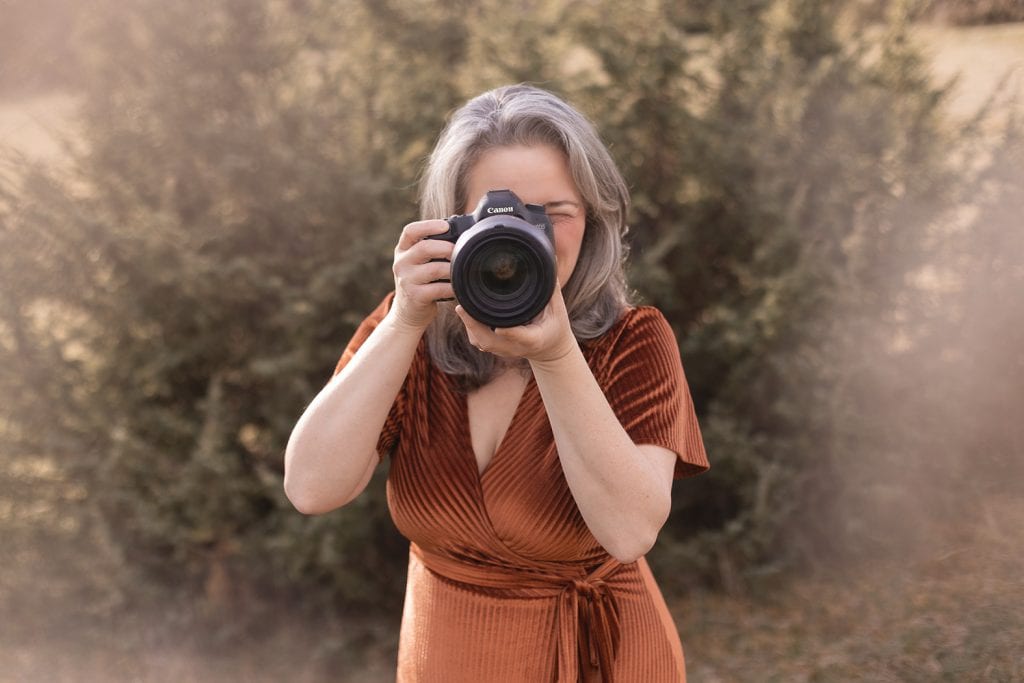 Sonja Auer mit Kamera im kupferfarbenen Samtkleid in einer weitläufigen Naturlandschaft bei Stuttgart.