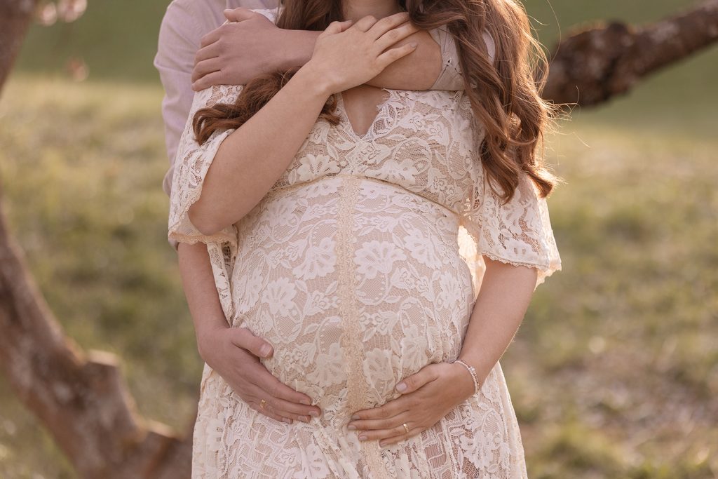 Paar hält gemeinsam den Babybauch inmitten rosa Kirschblüten – Babybauch Fotoshooting Stuttgart.