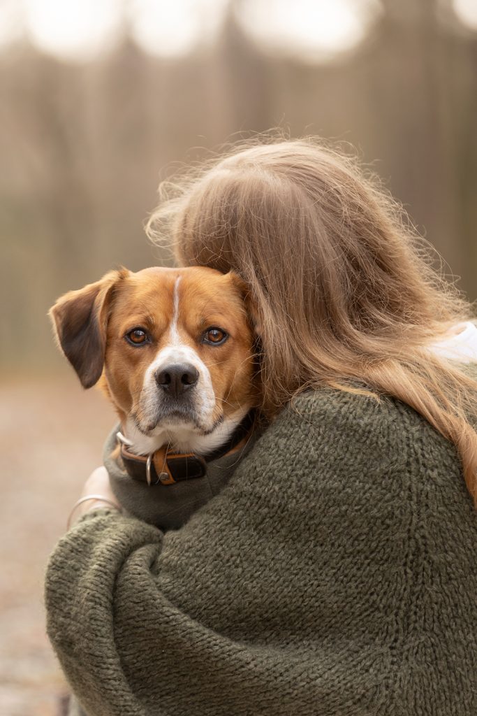 Frau umarmt ihren Hund, der direkt in die Kamera schaut – ein intensiver Moment voller Verbindung und Ausdruck.