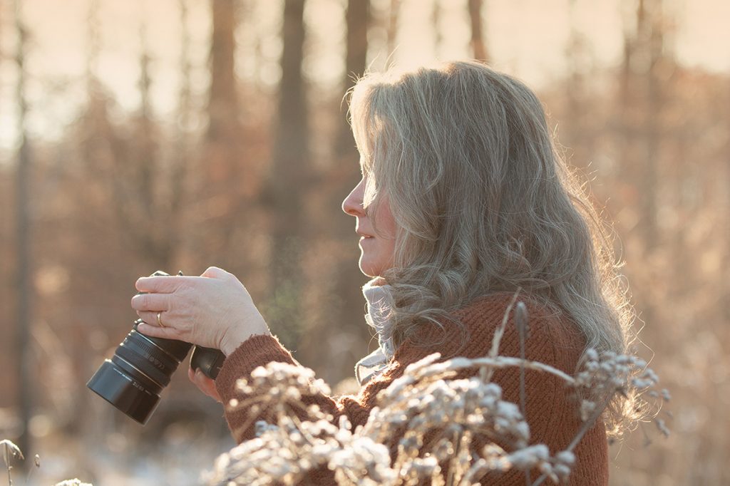 Sonja Auer outdoor Fotografin Stuttgart und Umgebung steht mit ihrer Kamera in der Hand im einer Schnee bedeckten Graslandschaft