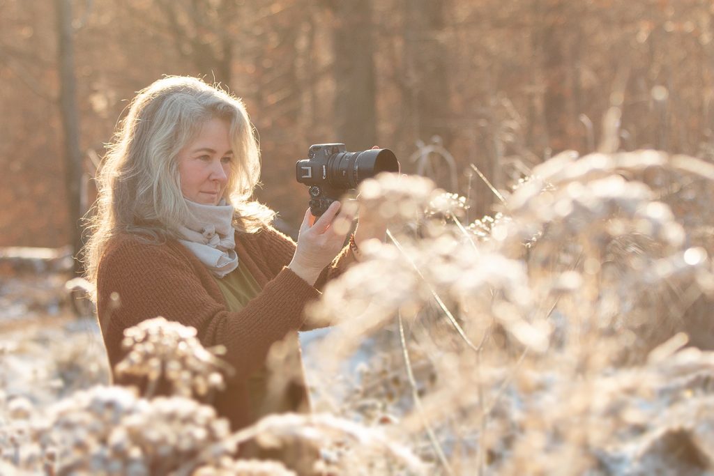 Sonja Auer outdoor Fotografin Stuttgart und Umgebung steht mit ihrer Kamera in der Hand im einer Schnee bedeckten Graslandschaft