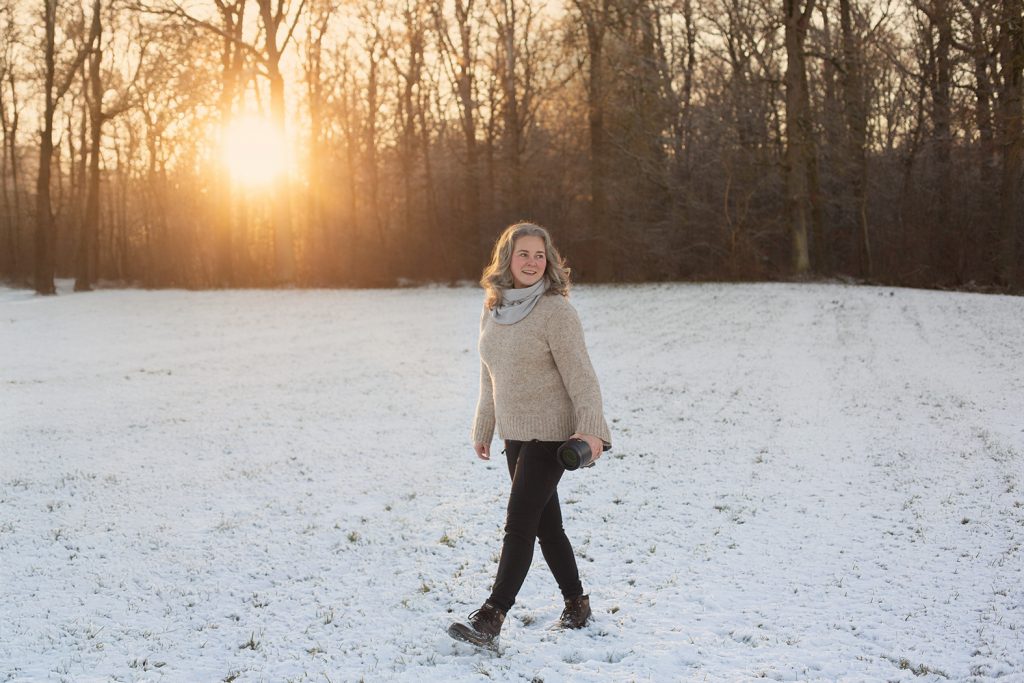 Sonja Auer die Fotografin geht mit ihrer Kamera in der Hand über eine verschneite Wiese im Abendlicht
