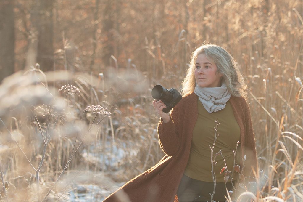 Sonja Auer outdoor Fotografin Stuttgart und Umgebung steht mit ihrer Kamera in der Hand im einer Schnee bedeckten Graslandschaft