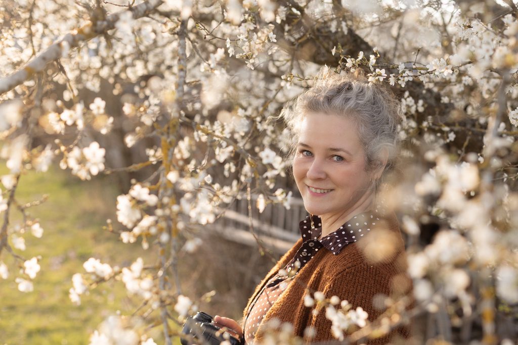 Fotografin aus Stuttgart mit Kamera zwischen weißen Mirabellenblüten