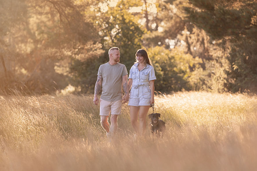 Paar mit Hund auf einer Wiese die im Sommer wind weht