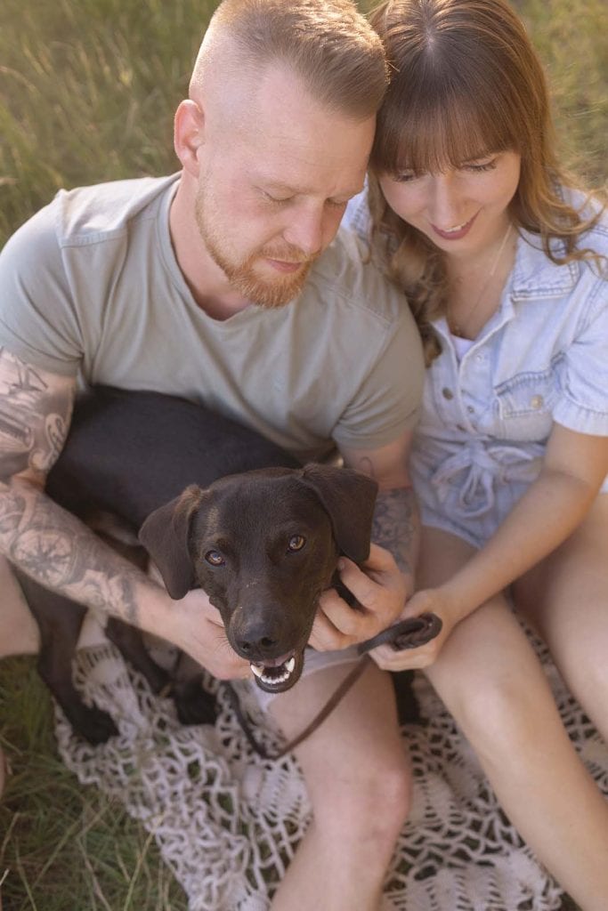 Paar sitzt gemeinsam mit seinem Hund auf einer Wiese und genießt einen innigen Moment – natürliche Outdoor-Fotografie in Stuttgart.